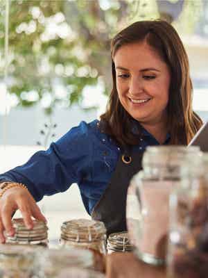Empresaria sonriente comprobando su inventario de té en grandes tarros de vidrio