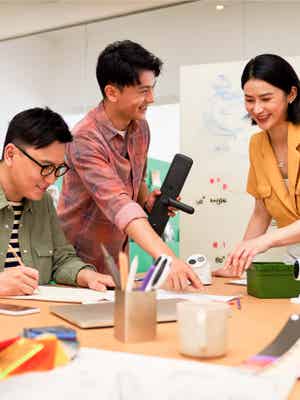 3 名商務青年一起工作。其中二人指著紙上的資料，另一人在紙上寫字。